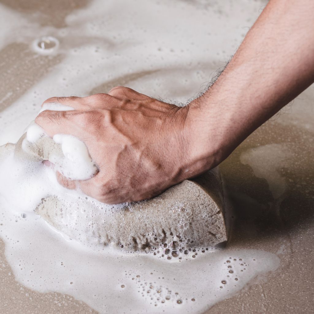 Close-up of hand scrubbing a concrete floor with a sponge.
